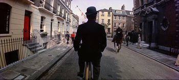 Movie still from “Around the World in 80 Days” (1956), directed by John Farrow – A man riding a bike down a street with people on it; Wide shot, High angle