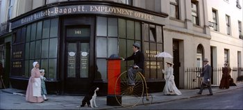 Movie still from “Around the World in 80 Days” (1956), directed by John Farrow – A man riding a bike down a street next to a mailbox; Wide shot, Low angle