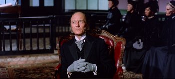 Movie still from “Around the World in 80 Days” (1956), directed by John Farrow – An older man sitting in a chair wearing gloves; Medium shot, Low angle