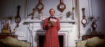 Movie still from “Around the World in 80 Days” (1956), directed by John Farrow – A man in a red and white coat standing in front of a fireplace holding an envelope; Medium shot, Low angle