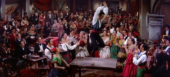 Movie still from “Around the World in 80 Days” (1956), directed by John Farrow – A group of people watching a man jump over a table in front of an audience; Wide shot, Low angle