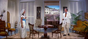 Movie still from “Around the World in 80 Days” (1956), directed by John Farrow – Two men and a woman are standing in front of a table with chairs; Wide shot, Low angle