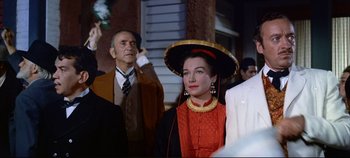 Movie still from “Around the World in 80 Days” (1956), directed by John Farrow – An old man and a woman in a red dress and a gold hat; Medium shot, Low angle