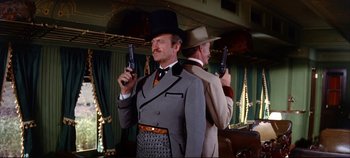 Movie still from “Around the World in 80 Days” (1956), directed by John Farrow – A man in a top hat holding a pair of pistols in front of another man in a suit; Medium shot, Low angle