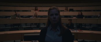Movie still from “Arrival” (2016), directed by Denis Villeneuve – A woman standing in front of a group of people in an auditorium; Medium shot, Over the shoulder angle
