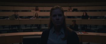 Movie still from “Arrival” (2016), directed by Denis Villeneuve – A woman standing in front of a group of people in a room; Medium shot, Over the shoulder angle