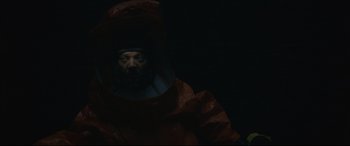 Movie still from “Arrival” (2016), directed by Denis Villeneuve – A man in a red suit is wearing a black helmet; Medium shot, Overhead angle