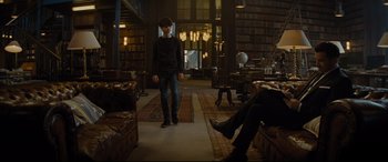 Movie still from “Artemis Fowl” (2020), directed by Kenneth Branagh – A man standing in front of a bookshelf in a library; Wide shot, High angle