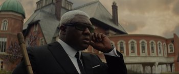 Movie still from “Artemis Fowl” (2020), directed by Kenneth Branagh – A man in a suit talking on a cell phone; Close Up shot, Low angle