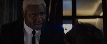 Movie still from “Artemis Fowl” (2020), directed by Kenneth Branagh – A person wearing a suit and tie; Close Up shot, Over the shoulder angle