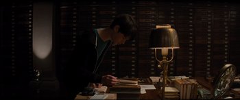 Movie still from “Artemis Fowl” (2020), directed by Kenneth Branagh – A person sitting at a table reading a book; Medium shot, High angle