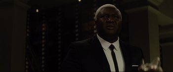 Movie still from “Artemis Fowl” (2020), directed by Kenneth Branagh – A man wearing a suit and tie in front of a wall; Close Up shot, Over the shoulder angle