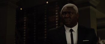 Movie still from “Artemis Fowl” (2020), directed by Kenneth Branagh – A man in a black suit and white tie; Close Up shot, Over the shoulder angle