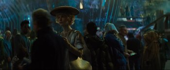Movie still from “Artemis Fowl” (2020), directed by Kenneth Branagh – A woman with a hat is standing in a crowd of people; Medium shot, Over the shoulder angle