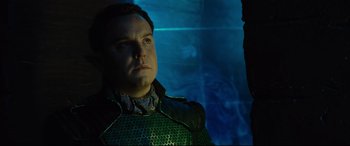Movie still from “Artemis Fowl” (2020), directed by Kenneth Branagh – A man in a green suit is standing in front of a blue wall; Close Up shot, Over the shoulder angle