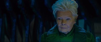 Movie still from “Artemis Fowl” (2020), directed by Kenneth Branagh – An older woman with white hair is wearing a green jacket; Close Up shot, Over the shoulder angle