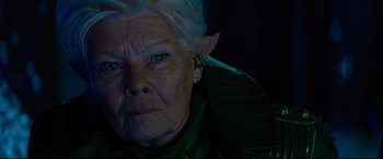 Movie still from “Artemis Fowl” (2020), directed by Kenneth Branagh – An older woman with a green jacket on; Close Up shot, Over the shoulder angle