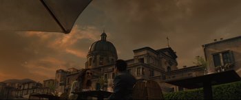 Movie still from “Artemis Fowl” (2020), directed by Kenneth Branagh – A man and a woman are sitting at a table outside; Extreme Wide shot, Low angle