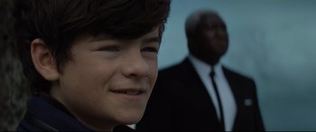 Movie still from “Artemis Fowl” (2020), directed by Kenneth Branagh – A young man smiling with a man in a suit behind him; Close Up shot, Over the shoulder angle