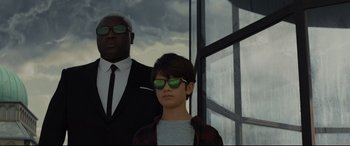 Movie still from “Artemis Fowl” (2020), directed by Kenneth Branagh – A man and a woman wearing sunglasses standing next to each other in front of a window; Medium shot, Low angle