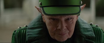 Movie still from “Artemis Fowl” (2020), directed by Kenneth Branagh – An older woman wearing a green hat and jacket; Close Up shot, Over the shoulder angle