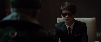 Movie still from “Artemis Fowl” (2020), directed by Kenneth Branagh – A man in a suit and sunglasses sitting in front of another man; Close Up shot, Over the shoulder angle