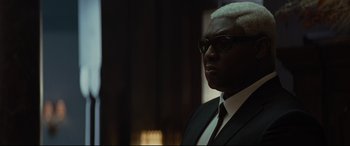 Movie still from “Artemis Fowl” (2020), directed by Kenneth Branagh – A man in a suit and tie looking to his left; Close Up shot, Over the shoulder angle