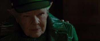 Movie still from “Artemis Fowl” (2020), directed by Kenneth Branagh – An older woman wearing a green leather jacket and hat; Close Up shot, Over the shoulder angle
