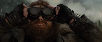 Movie still from “Artemis Fowl” (2020), directed by Kenneth Branagh – A man with a beard wearing goggles and a leather jacket; Close Up shot, Low angle