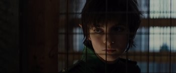 Movie still from “Artemis Fowl” (2020), directed by Kenneth Branagh – A young boy looking through the bars of a cage; Close Up shot, Over the shoulder angle