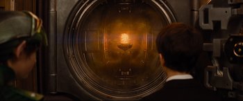 Movie still from “Artemis Fowl” (2020), directed by Kenneth Branagh – A man looking into an industrial machine with a bright light coming out of it; Medium shot, High angle
