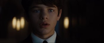 Movie still from “Artemis Fowl” (2020), directed by Kenneth Branagh – A young boy in a suit and tie looking at the camera; Close Up shot, Over the shoulder angle