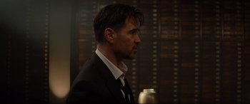 Movie still from “Artemis Fowl” (2020), directed by Kenneth Branagh – A man wearing a suit and tie standing in front of a wall; Close Up shot, Over the shoulder angle