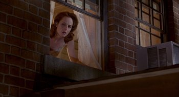 Movie still from “As Good as It Gets” (1997), directed by James L. Brooks – A woman looking out of a window in a brick building; Medium shot, Low angle