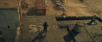 Movie still from “Assassin's Creed” (2016), directed by Justin Kurzel – A man riding a bike down the side of a street; Extreme Wide shot, Overhead angle