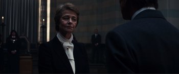 Movie still from “Assassin's Creed” (2016), directed by Justin Kurzel – An older woman wearing a suit and tie; Close Up shot, Over the shoulder angle