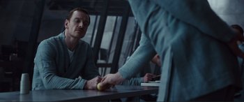Movie still from “Assassin's Creed” (2016), directed by Justin Kurzel – A man sitting at a table holding an apple in his hand; Medium shot, Over the shoulder angle