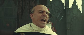 Movie still from “Assassin's Creed” (2016), directed by Justin Kurzel – A man with a bald head wearing a priest's outfit; Close Up shot, Low angle