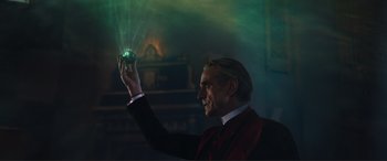 Movie still from “Assassin's Creed” (2016), directed by Justin Kurzel – A man in a suit and tie holding up a crystal ball; Medium shot, Low angle