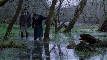 Movie still from “Assassins” (1995), directed by Richard Donner – Two people walking through a flooded area near trees; Wide shot, Over the shoulder angle