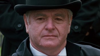 Movie still from “Assassins” (1995), directed by Richard Donner – An older man wearing a black hat and a white shirt; Close Up shot, Low angle