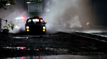 Movie still from “Assassins” (1995), directed by Richard Donner – A car is driving down the street in the dark; Wide shot, Low angle