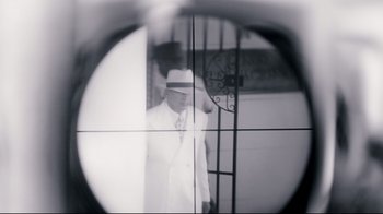 Movie still from “Assassins” (1995), directed by Richard Donner – A man wearing a white suit and a white hat is looking through a rifle scope; Extreme Close Up shot, Over the shoulder angle