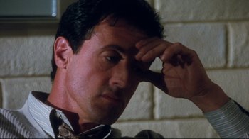 Movie still from “Assassins” (1995), directed by Richard Donner – A man with a hand on his forehead looking down; Close Up shot, High angle