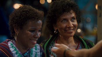 Movie still from “Assassins” (1995), directed by Richard Donner – Two women are sitting next to each other and smiling; Close Up shot, Over the shoulder angle