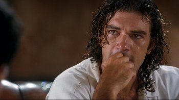 Movie still from “Assassins” (1995), directed by Richard Donner – A person sitting down with his hand to his face; Close Up shot, Low angle