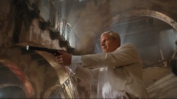 Movie still from “Assassins” (1995), directed by Richard Donner – A man holding a gun while standing next to a wall; Medium shot, Low angle