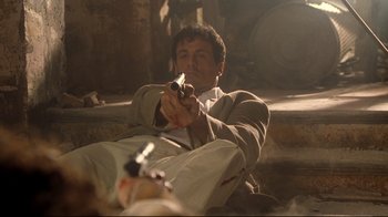 Movie still from “Assassins” (1995), directed by Richard Donner – A man sitting on the ground holding a gun in his hand; Medium shot, Low angle
