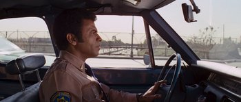 Movie still from “Assault on Precinct 13” (1976), directed by John Carpenter – A man sitting in the driver's seat of a car; Medium shot, Over the shoulder angle