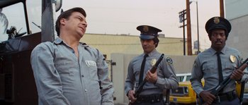 Movie still from “Assault on Precinct 13” (1976), directed by John Carpenter – A police officer holding a gun next to a man in a prison uniform; Medium shot, Low angle